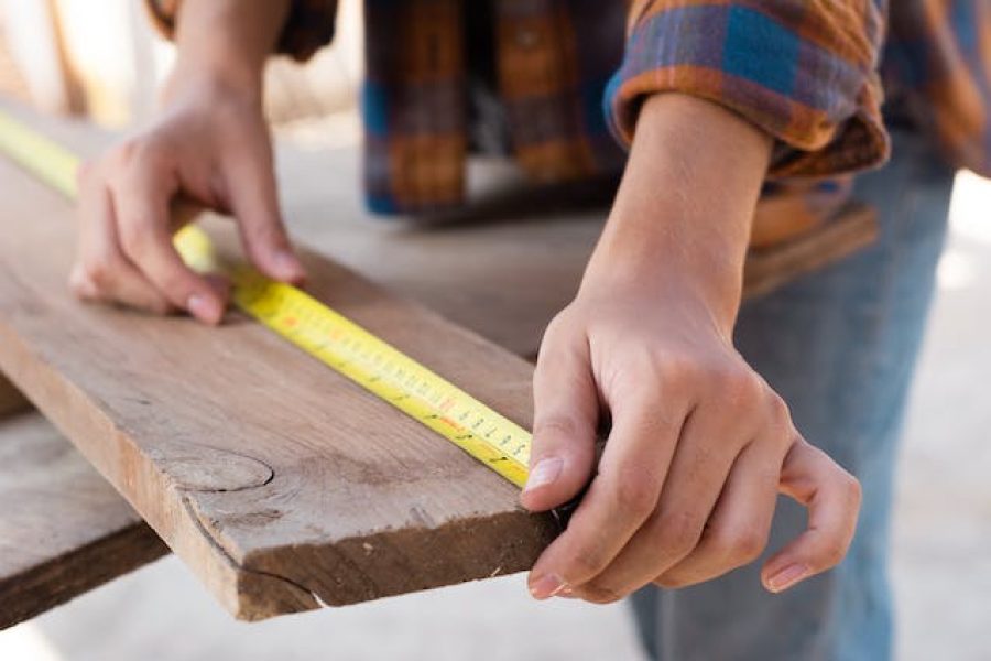 A contractor using a measuring tape on a plank of wood