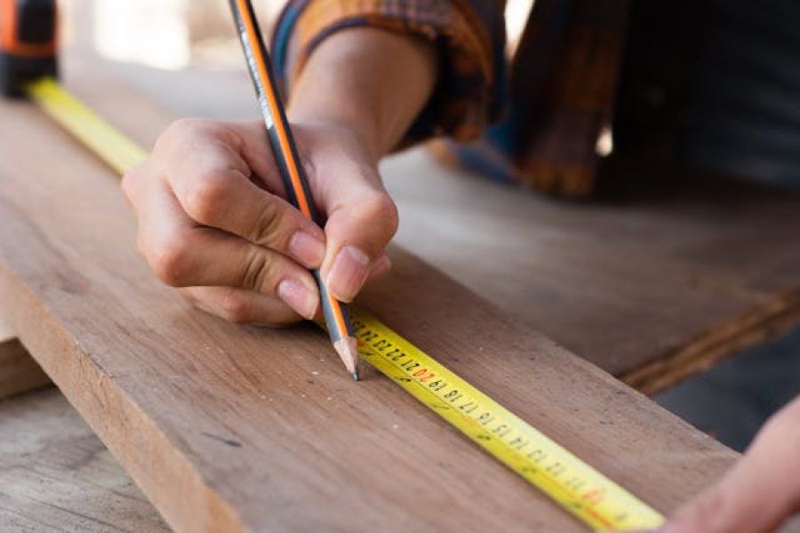 A person using a pencil and ruler to mark something on a piece of wood
