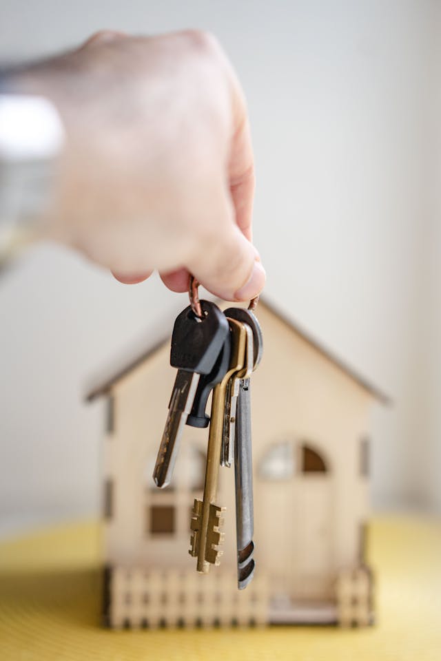 Person holding house keys in front of a home figurine