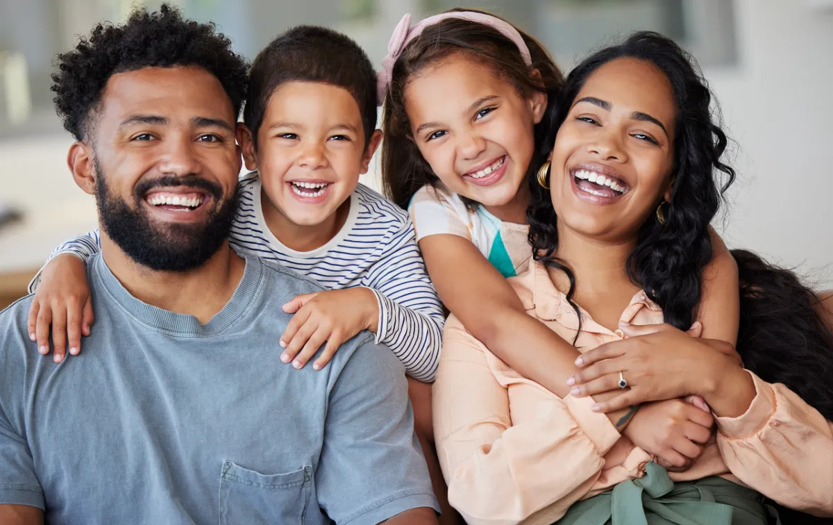 A young family of four smiling hugging one another