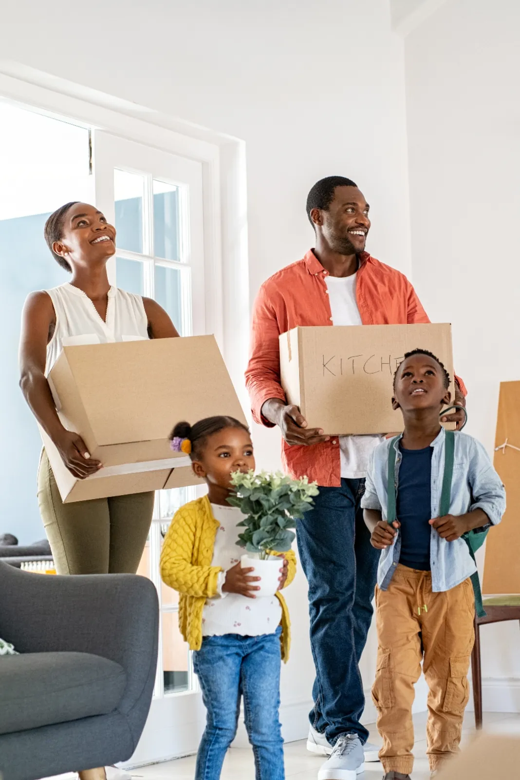 A smiling couple and two children carrying boxes into their new home