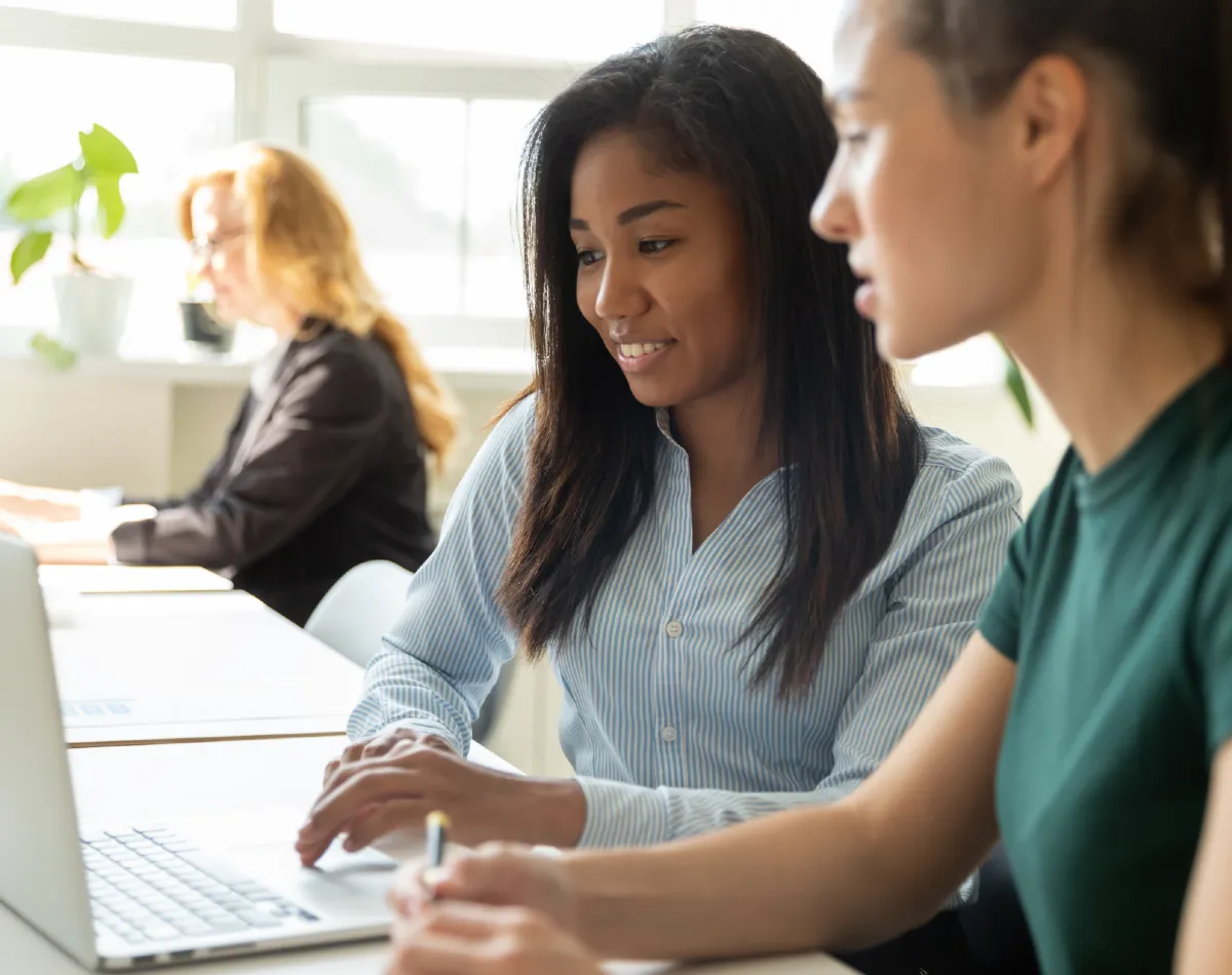 Two young women working together on a laptop in an office