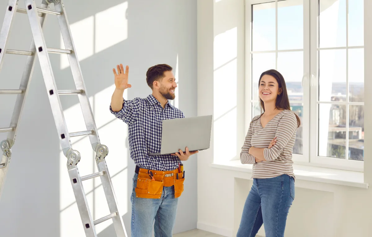 A man with a toolbelt smiling and gesturing to a woman in an apartment