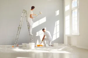 Two male painters dressed in white painting an interior wall in an apartment