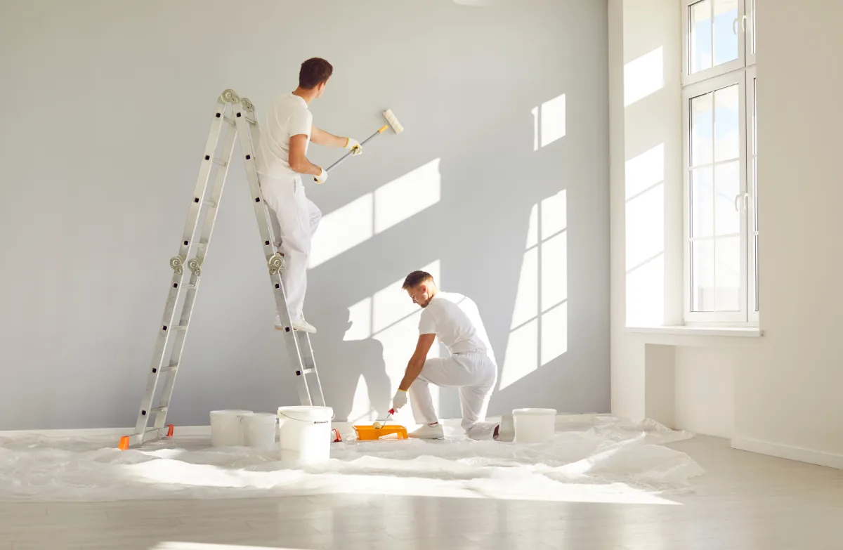 Two male painters dressed in white painting an interior wall in an apartment