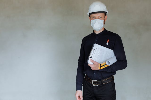 a contractor in a mask and hard hat holding a clipboard