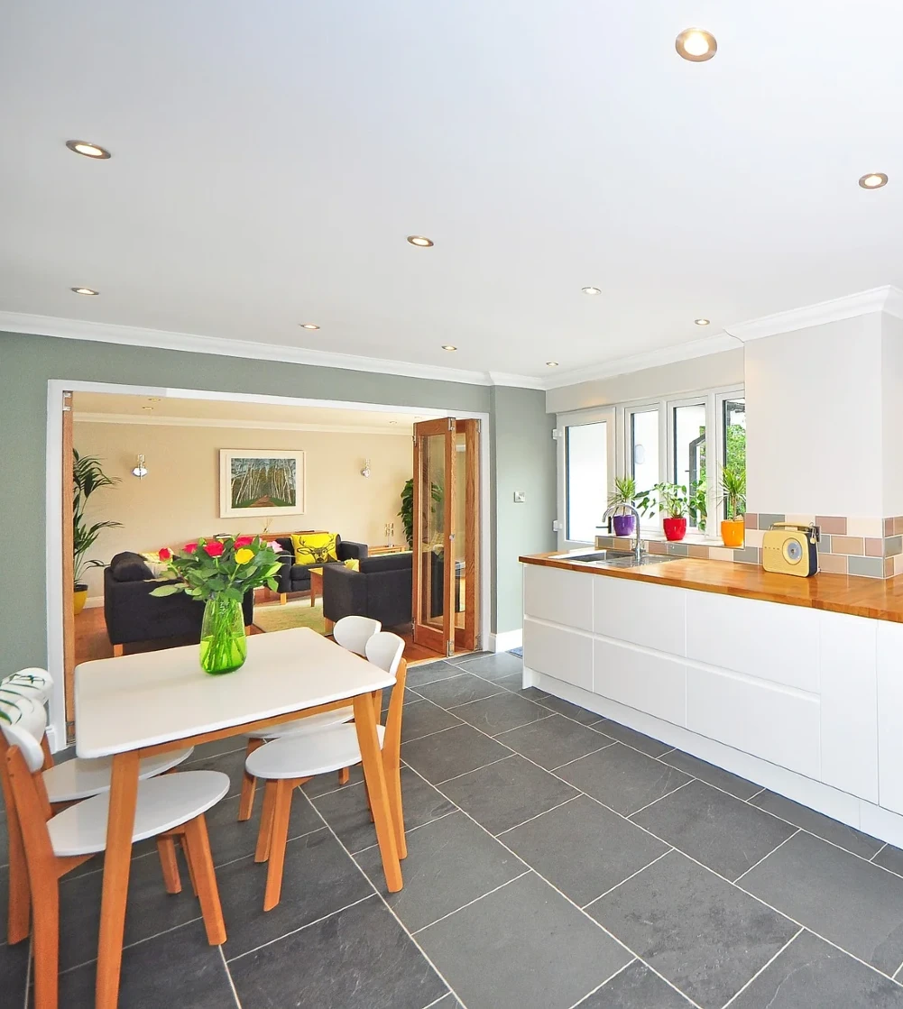 A kitchen with grey flooring, white cabinets and light wood accents