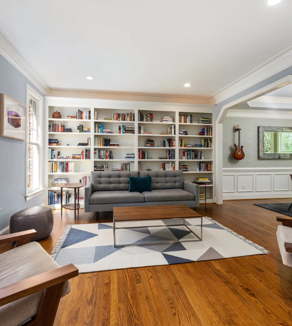 A living room with a built in book case, blue walls and a dark wood flooring
