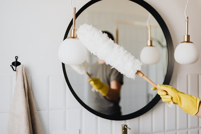 a person in yellow cleaning gloves using a feather duster on a mirror