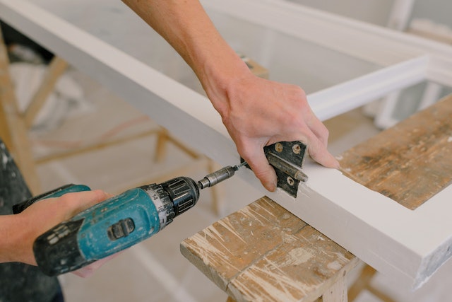 contractor using a drill to fix a window’s hinge