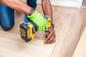 person in green work gloves using electric drill on piece of wood