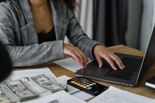person on their laptop with cash and accounting statements next to them on their desk