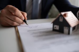 person signing a document with a home figurine one top