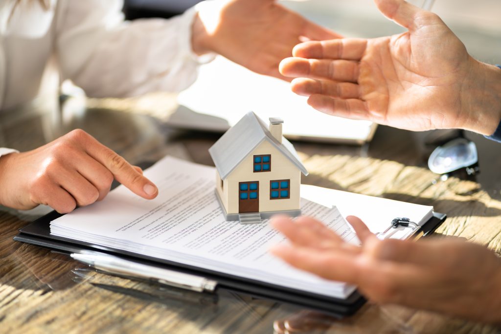 a house figurine resting on a contract between two people
