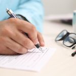 person-signing-papers-with-glasses-on-table